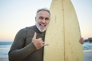 Image showing Senior man, with surfboard and at beach smile, happy and at sunset with swimwear on a holiday and vacation. Portrait, shaka and older male surfer, hand sign and at seaside surfing while on a trip.