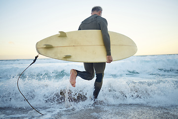 Image showing Man is at the beach in summer, with surfboard while in the ocean waves for sport and fitness during sunrise. Mature surfer while running, in a wet suit to surf and enjoy the sea water for health.