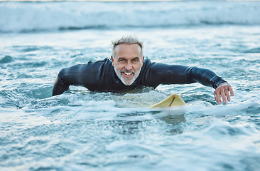 Image showing Senior man, water and sports surfer on a beach with smile training for fitness and health or hobby in the outdoors. Elderly male paddling on surfboard for healthy exercise in the ocean waves at sea