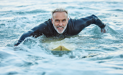 Image showing Man at beach during summer, in the ocean and surfing with surfboard for sport and fitness in a portrait. Mature, smile and surf in a wet suit for health and happy in sea water and outdoor.