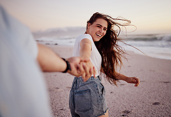 Image showing Happy, woman and hand holding at the beach of a couple having fun together with love. Happiness of a girlfriend and boyfriend smile on sea sand near ocean waves at sunset during a summer travel