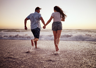 Image showing Couple, beach and running, holding hands in waves at sunset on romantic holiday. Love, freedom and a man and woman on ocean vacation together. Sea, sunset and romance, happy guy and girl run in water