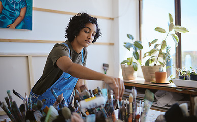 Image showing Art, creative and painter with decision for brush while working on a painting in a studio for work. Indian woman, artist or designer picking a tool for oil paint job on a table in a workshop