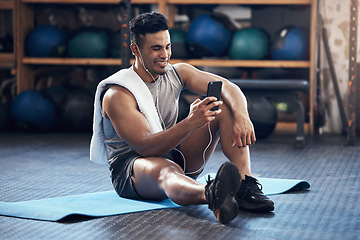 Image showing Man, exercise and phone on social media with smile rest on floor in gym during training session. Guy, wellness and smartphone take break during workout for fitness, health and sport with happiness