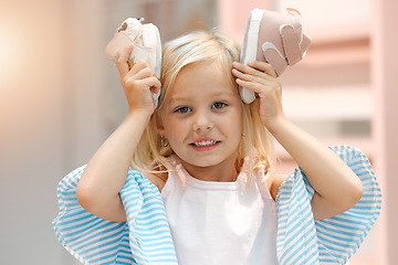 Image showing Children, fashion and clothes with shoes in girl hands against her head while shopping in a retail store. Kids, cute and choice with a female child deciding what shoe to buy for her wardrobe