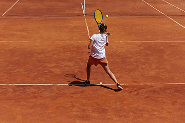 Image showing A young girl showing professional tennis skills in a competitive match on a sunny day, surrounded by the modern aesthetics of a tennis court.