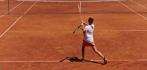 Image showing A young girl showing professional tennis skills in a competitive match on a sunny day, surrounded by the modern aesthetics of a tennis court.