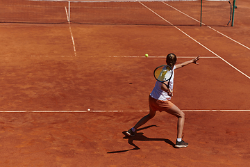 Image showing A young girl showing professional tennis skills in a competitive match on a sunny day, surrounded by the modern aesthetics of a tennis court.