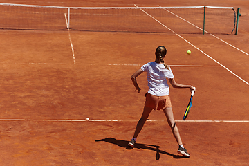 Image showing A young girl showing professional tennis skills in a competitive match on a sunny day, surrounded by the modern aesthetics of a tennis court.