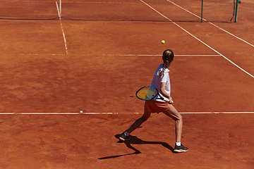 Image showing A young girl showing professional tennis skills in a competitive match on a sunny day, surrounded by the modern aesthetics of a tennis court.