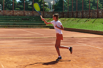 Image showing A young girl showing professional tennis skills in a competitive match on a sunny day, surrounded by the modern aesthetics of a tennis court.