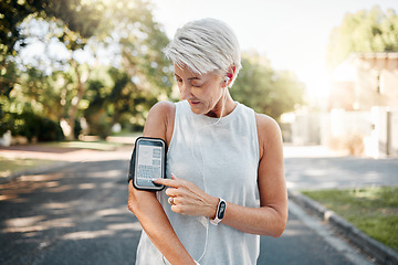 Image showing Senior woman, fitness and phone armband listening to music for morning run in an urban street outdoors. Active elderly female runner checking smartphone to monitor training exercise or navigation