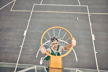 Image showing Portrait of basketball player hanging on net on a basketball court. Young man playing basketball outside doing slam dunk and jumping to score a point. Motivation to win and have fun in sports game