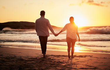 Image showing Sunset, couple holding hands and walking by the beach with a beautiful twilight. Love, romance and happy man and woman spending time together with affection by ocean, sea and sandy shore on holiday.