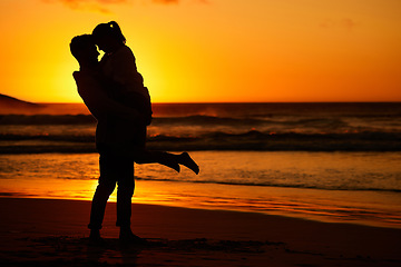 Image showing Couple, beach and sunset with a man and woman hugging on the coast with a golden view in the background. Love, silhouette and ocean with a male and female embracing on the sand by the sea for travel