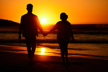 Image showing Ocean sunset, couple walking and beach water at night or woman and man love holding hands at sea summer vacation. Travel together, honeymoon silhouette and bonding on holiday sky sunlight in nature