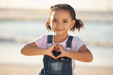 Image showing Girl at beach make heart sign with hands, happy and smile against blurred nature background. Young female child with expression of happiness, makes love icon, gesture with fingers by the ocean or sea