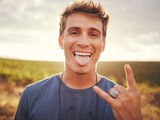 Image showing Man, hands and portrait of rock sign for travel tour or vacation in the countryside and nature outdoors. Happy, excited young male traveler, rocker or musician with hand gesture and tongue out