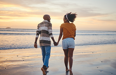 Image showing Black couple, holding hands and on beach with sunset for romance, celebrate relationship or holiday together. Love, happy man and woman bare feet, relax or smile on romantic seaside vacation or break