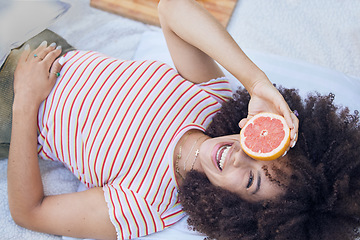 Image showing Fruit, picnic and summer with a happy black woman holding a grapefruit while lying on a blanket outdoor. Food, health and wellness with a female laughing or joking while outside to relax from above