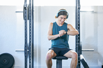 Image showing Fitness, man checking time and exercise for sports training monitoring workout while sitting on a bench at the gym. Athletic sport male looking at watch while resting on equipment indoors
