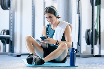 Image showing Man check social media in gym, workout music playlist on smartphone and typing online conversation. Happy young athlete sitting on floor, sports health application and fitness lifestyle technology
