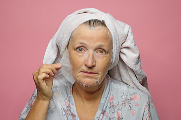 Image showing senior woman applying a facial mask napkin