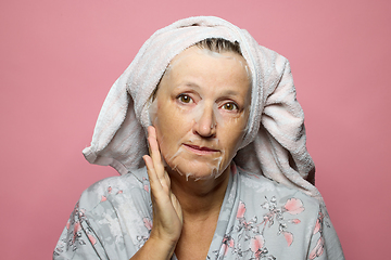 Image showing senior woman applying a facial mask napkin