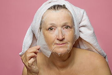 Image showing senior woman applying a facial mask napkin