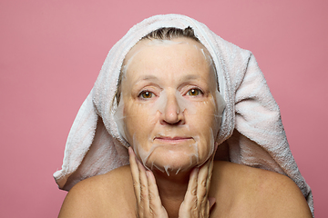 Image showing senior woman applying a facial mask napkin