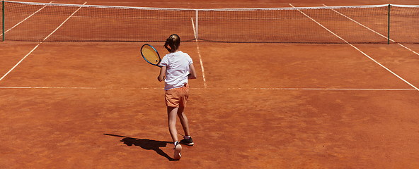 Image showing A young girl showing professional tennis skills in a competitive match on a sunny day, surrounded by the modern aesthetics of a tennis court.