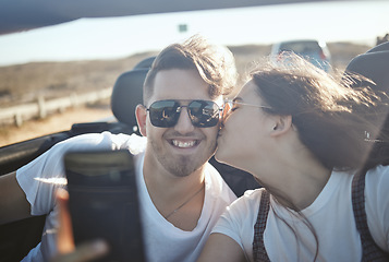 Image showing Selfie, kiss and road trip with a real couple driving on the one road for vacation, honeymoon or romance. Love, happy and kissing with a young man and woman taking a photograph while sitting in a car