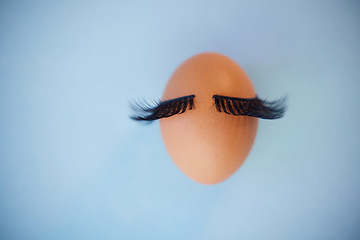 Image showing Beauty, makeup and eyelashes with an egg on a blue background in studio with mockup. Cosmetics, mascara or abstract with an embryo and fake lashes with product placement for marketing or advertising