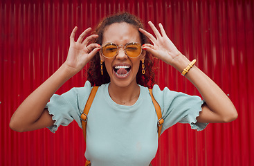 Image showing Funny, happy portrait of black woman face and smile with her tongue out with designer fashion sunglasses on red background. Girl with crazy comic expression, modern hair style and trendy accessories