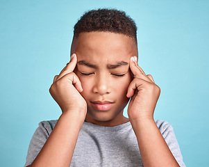 Image showing Child with headache, stress and mental health problem or fatigue pain on blue studio background. Frustrated african american kid, depressed boy and angry youth with fingers massaging temples of head