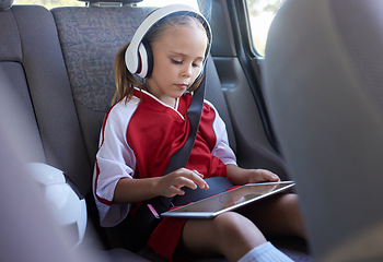 Image showing Child with tablet, headphones and safety belt in the car going home after soccer match, game or practice. Young girl in sports gear playing educational games online on tech device after training