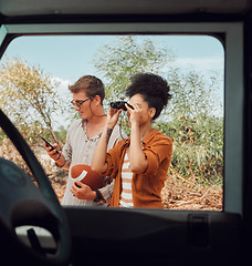 Image showing Window, car and diversity couple on road trip journey to explore Australia safari, countryside or outdoor nature. Binocular, transportation adventure and man streaming football game on mobile phone