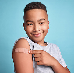 Image showing .Child black, band aid and happy kid with vaccine, in blue studio background and relax with smile or joyful. Portrait, boy and adhesive bandage with arm bruise, confident and vaccination for health.