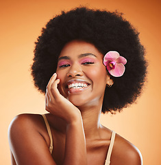 Image showing Face, beauty and black woman with flower in afro hair on orange studio background. Portrait, skincare and happy woman or female model from Nigeria in pink makeup, cosmetics and orchid in healthy hair