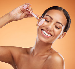 Image showing Jade roller, skincare and woman with massage for face beauty against an orange studio background. Happy, young and healthy model with a dermatology product for facial wellness and care with a smile