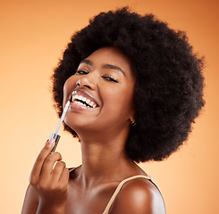 Image showing Lipgloss, smile and black woman excited about makeup against an orange studio background. Face portrait of a young African girl model with lipstick and cosmetic beauty product for care of lips