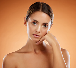 Image showing Skincare, beauty and portrait with hand pose and serious face of beautiful woman with glowing body. Model girl at orange background with natural, young and cosmetic feeling on skin in studio.