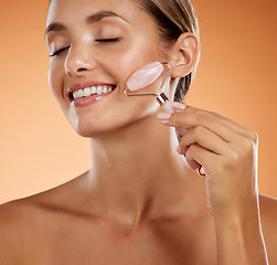 Image showing Skincare, cosmetics and woman with face roller, natural beauty and glow with confidence, smile and firm or anti aging in brown studio background. Makeup, girl or body care, wellness or facial massage