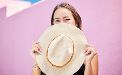 Image showing Travel, fashion and summer hat with a woman tourist in the city on a pastel color pink wall background. Happy, holiday and tourist with a female traveler covering her face with a sunhat in town