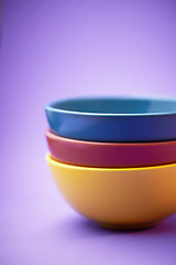 Image showing Color, container and group of ceramic bowl, kitchen equipment or plastic plate tower for soup, cereal or breakfast food. Colorful stack of blue, yellow and maroon objects on purple background studio