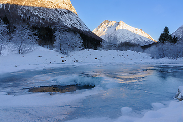 Image showing A frozen river with snow and mountains in the background