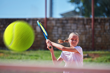 Image showing A young girl showing professional tennis skills in a competitive match on a sunny day, surrounded by the modern aesthetics of a tennis court.