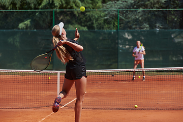 Image showing Young girls in a lively tennis match on a sunny day, demonstrating their skills and enthusiasm on a modern tennis court.