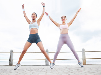 Image showing Jumping jack, fitness and women training cardio, happy with workout and smile during exercise in the city by the ocean. Young friends with energy for sports collaboration and stretching in the street