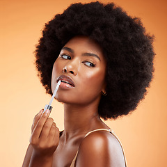 Image showing Black woman, afro and natural beauty lip gloss treatment for a healthy, shiny and transparent tint. Cosmetics, apply and beautiful face of African model holding makeup tool at orange background.